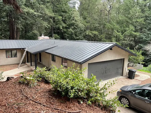 Gray standing-seam metal roof covering a home and attached garage surrounded by redwood trees